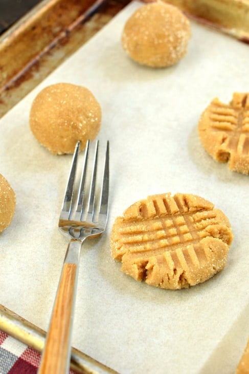 Peanut butter cookie balls on a parchment paper lined baking sheet. Fork on the side, with fork marks in some of the cookies.