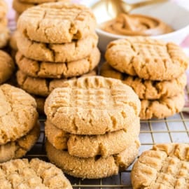 Stacks of peanut butter cookies with crisscross tops cool on a rack, with a bowl of peanut butter behind—perfect inspiration for your next peanut butter cookies recipe.