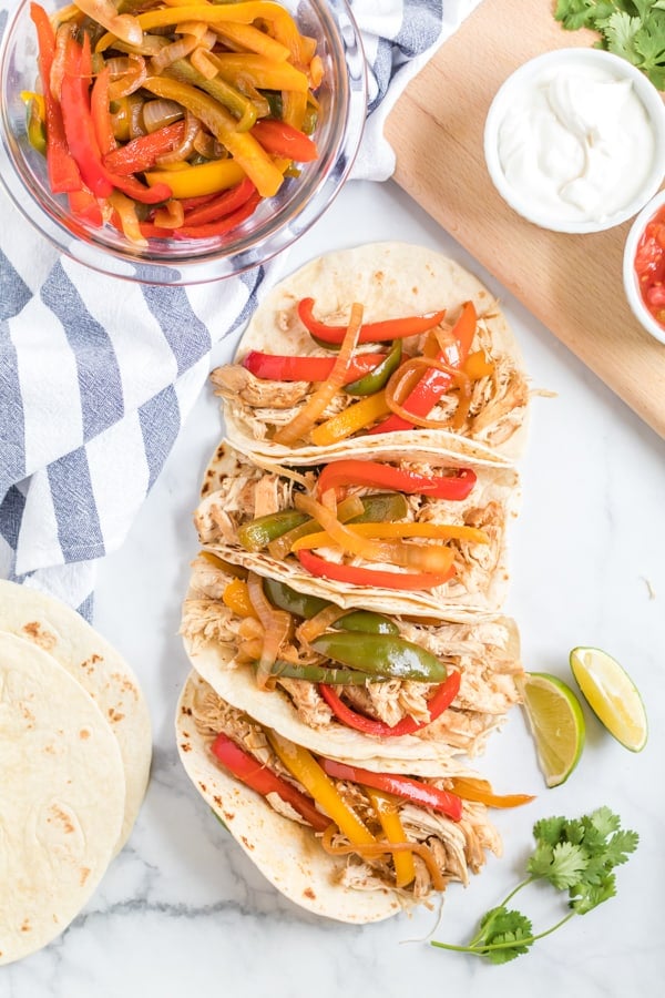Chicken fajitas on flour tortillas stacked and in a row on a marble countertop.