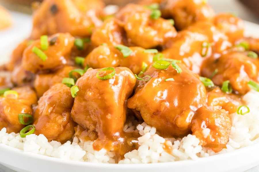 Close up of glazed orange chicken with white rice on a white plate.