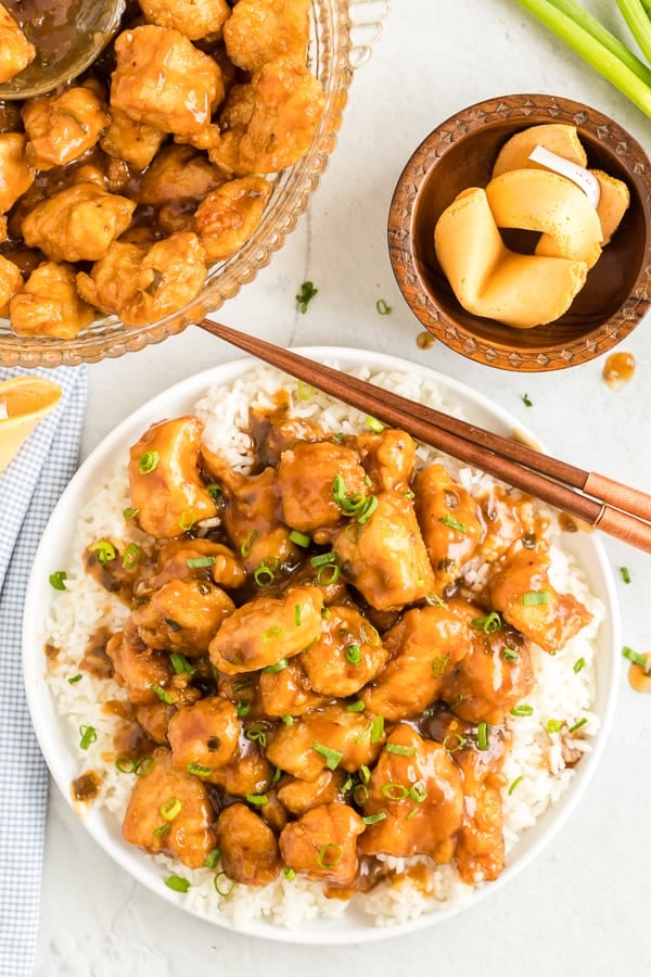 Glazed chicken with orange sauce on a white plate with white rice and chopsticks.