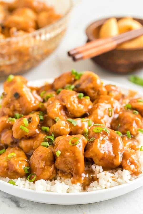 Sweet and Tangy glazed orange chicken on a bowl of rice with green onion and chopsticks