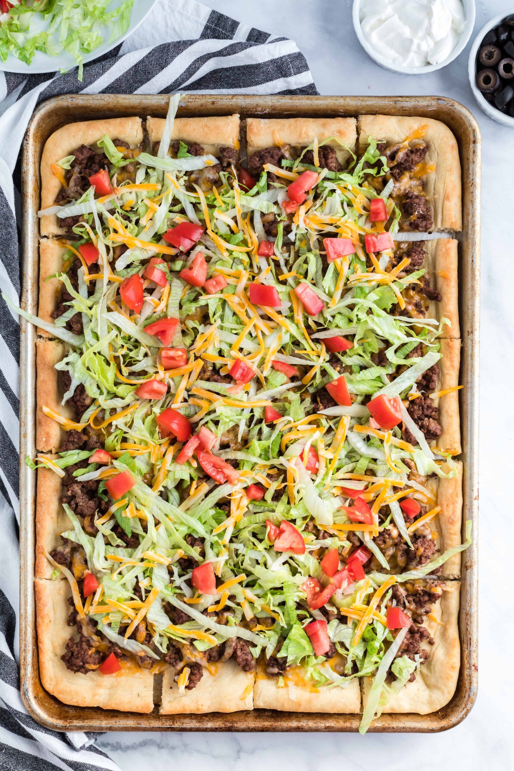 Baked taco pizza in a metal pan topped with lettuce and tomatoes.