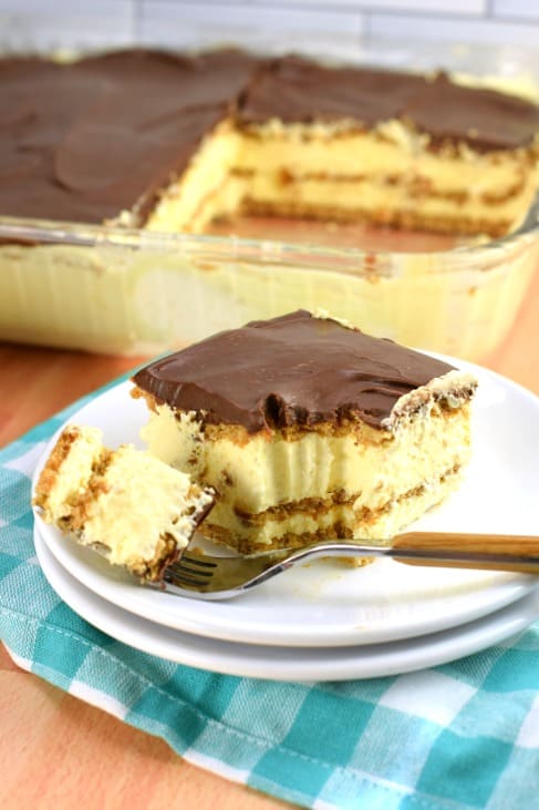 Slice of chocolate eclair cake on a stack of two white plates, with one forkful removed.