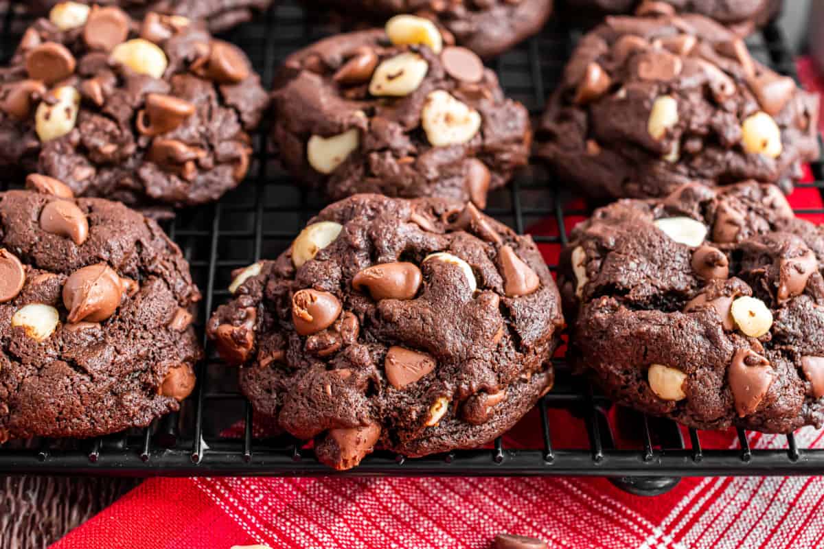 Chocolate cookies with macadamia nuts stacked on a wire cooling rack.