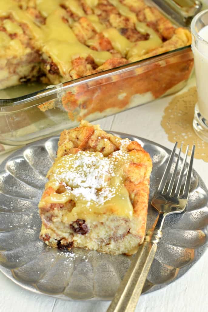 Slice of bread pudding on a silver plate topped with lemon sauce and powdered sugar.