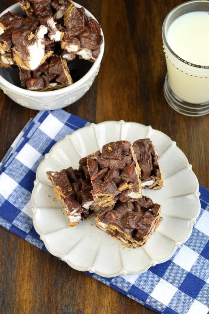 No Bake Indoor S'mores Bars with just 3 ingredients! Easy to make, no campfire needed. No Bake Indoor S'mores Bars with just 3 ingredients cut into squares on a white plate with blue napkin.