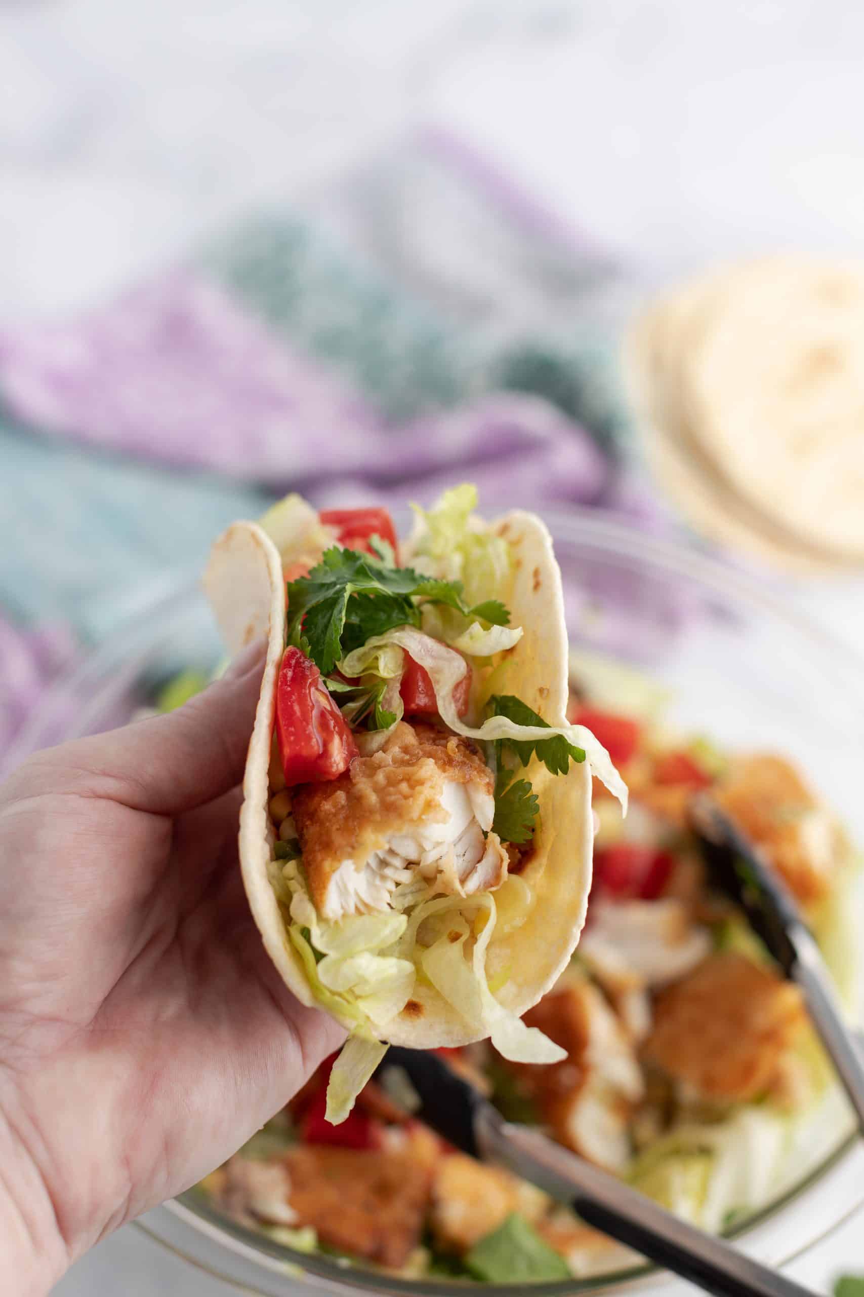 Fish taco on a flour tortilla being held up for a bite.