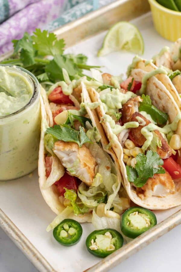 Fish Tacos on flour tortillas with lettuce, tomato, jalapeno, avocado sauce, and lime