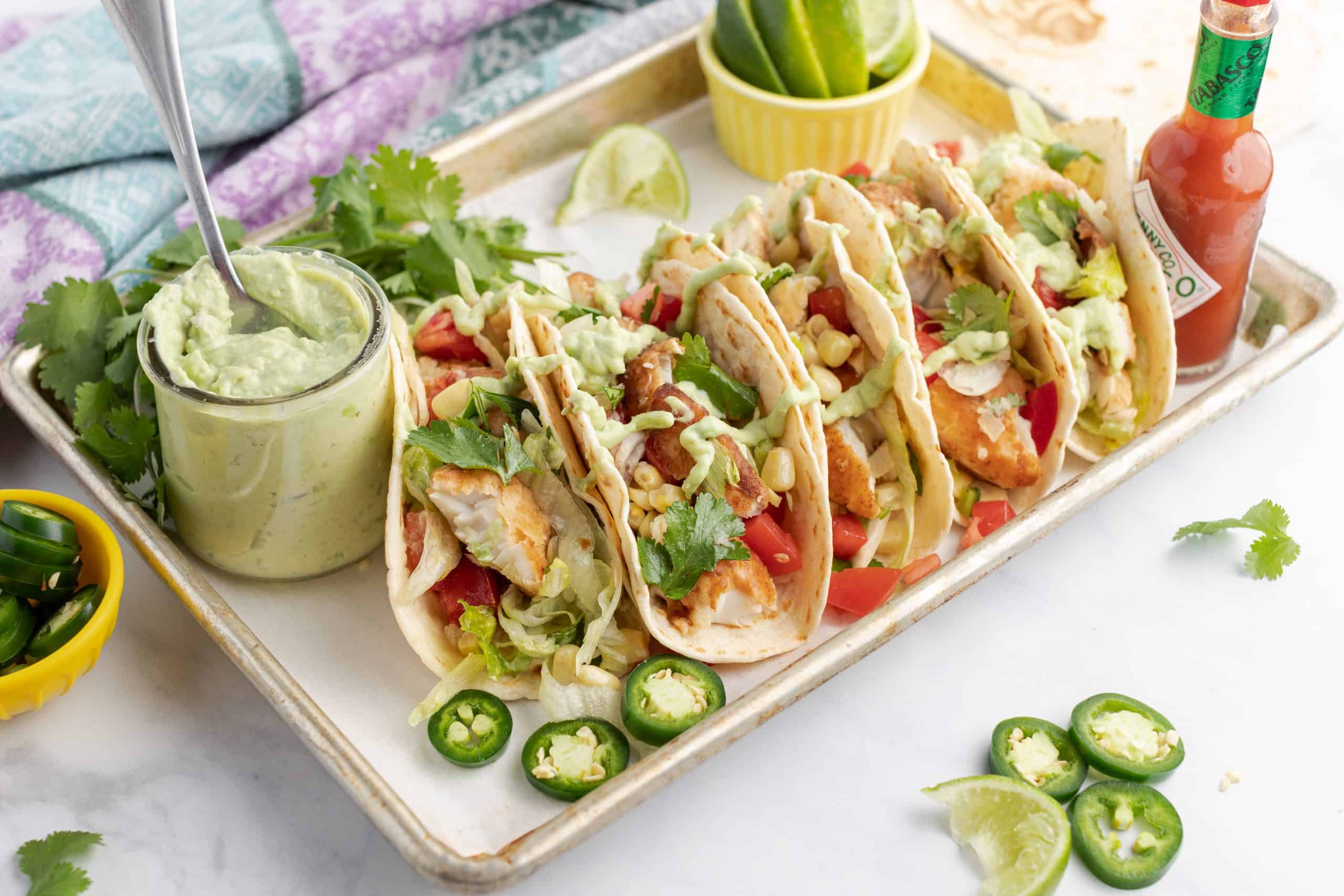 Tray with fish tacos, jar of avocado sauce, tabasco, and sliced jalapenos.