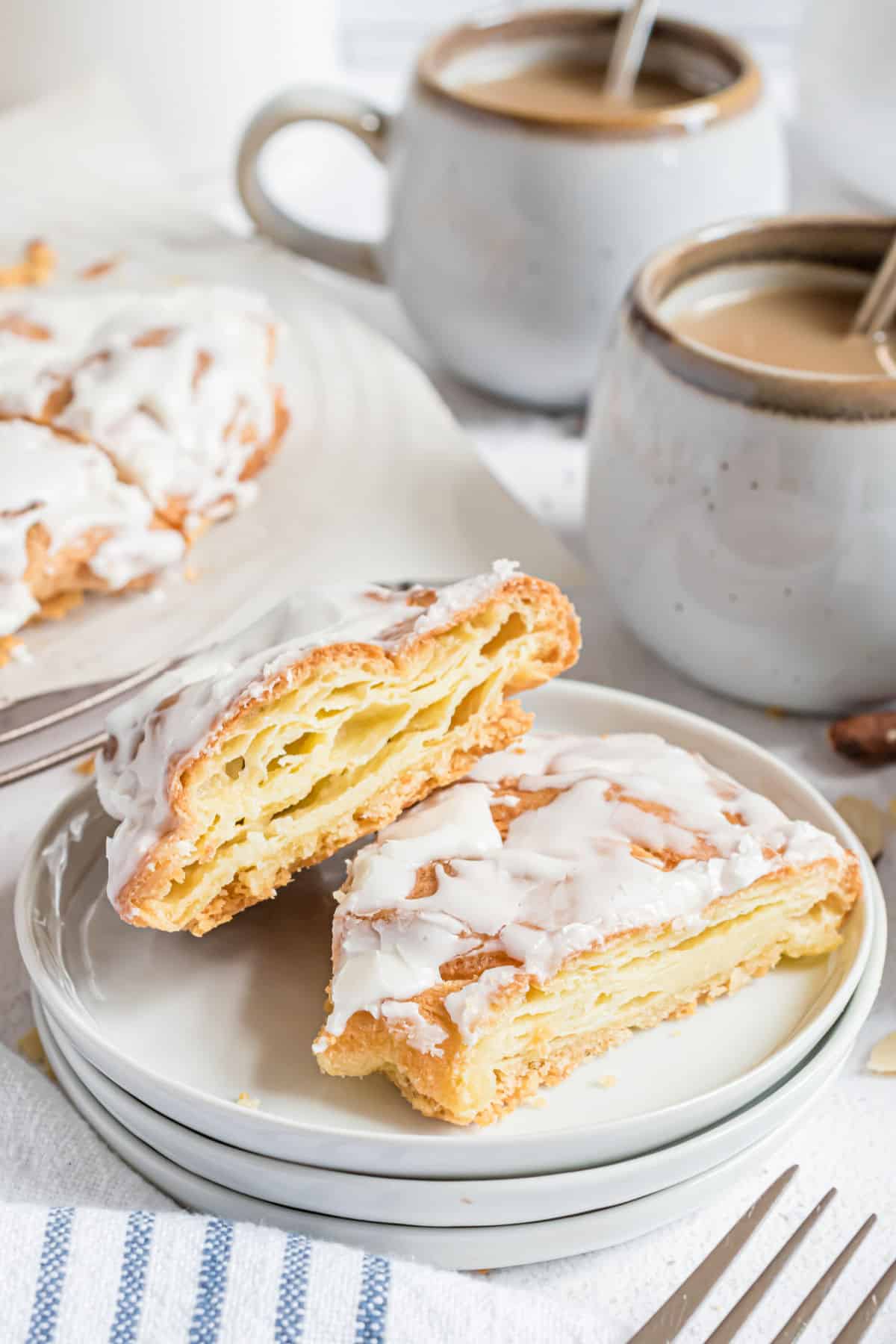 Two slices of almond kringle on a stack of white plates.