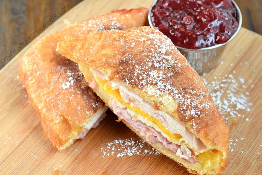 Monte cristo sandwich cut in half on a wooden cutting board with a side of raspberry jam.