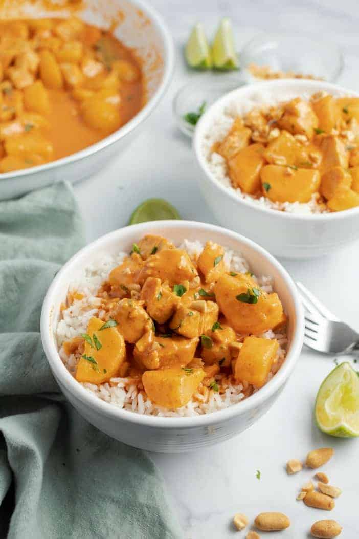 Two bowls of rice with thai curry topped with cilantro, lime, and peanuts