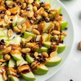 Apple nachos on a plate with green apple slices, caramel, chocolate, and melted marshmallow.