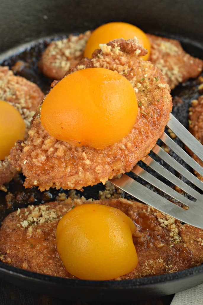 Cast iron skillet with a metal spatula lifting a shake and bake cooked pork chop with peaches.