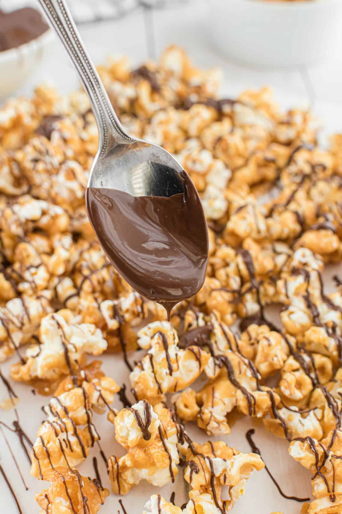 Caramel corn being drizzled with chocolate from a spoon.