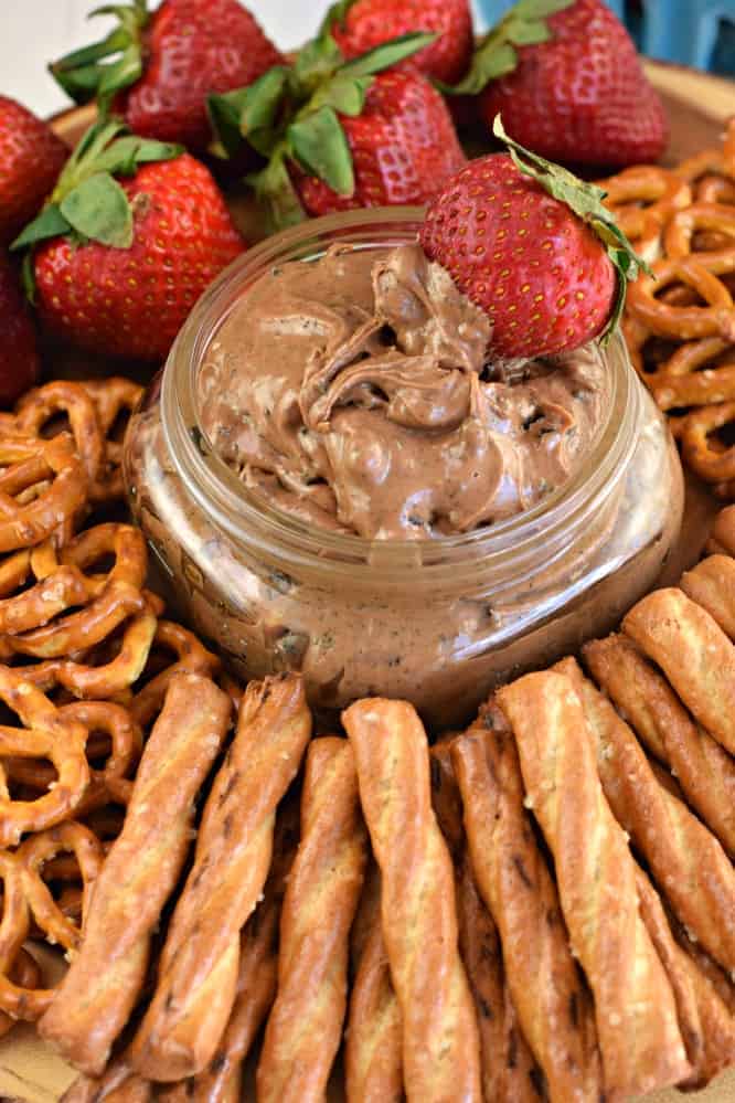 Oreo peanut butter dip in a small glass mason jar with strawberries and pretzels around it on a serving tray.