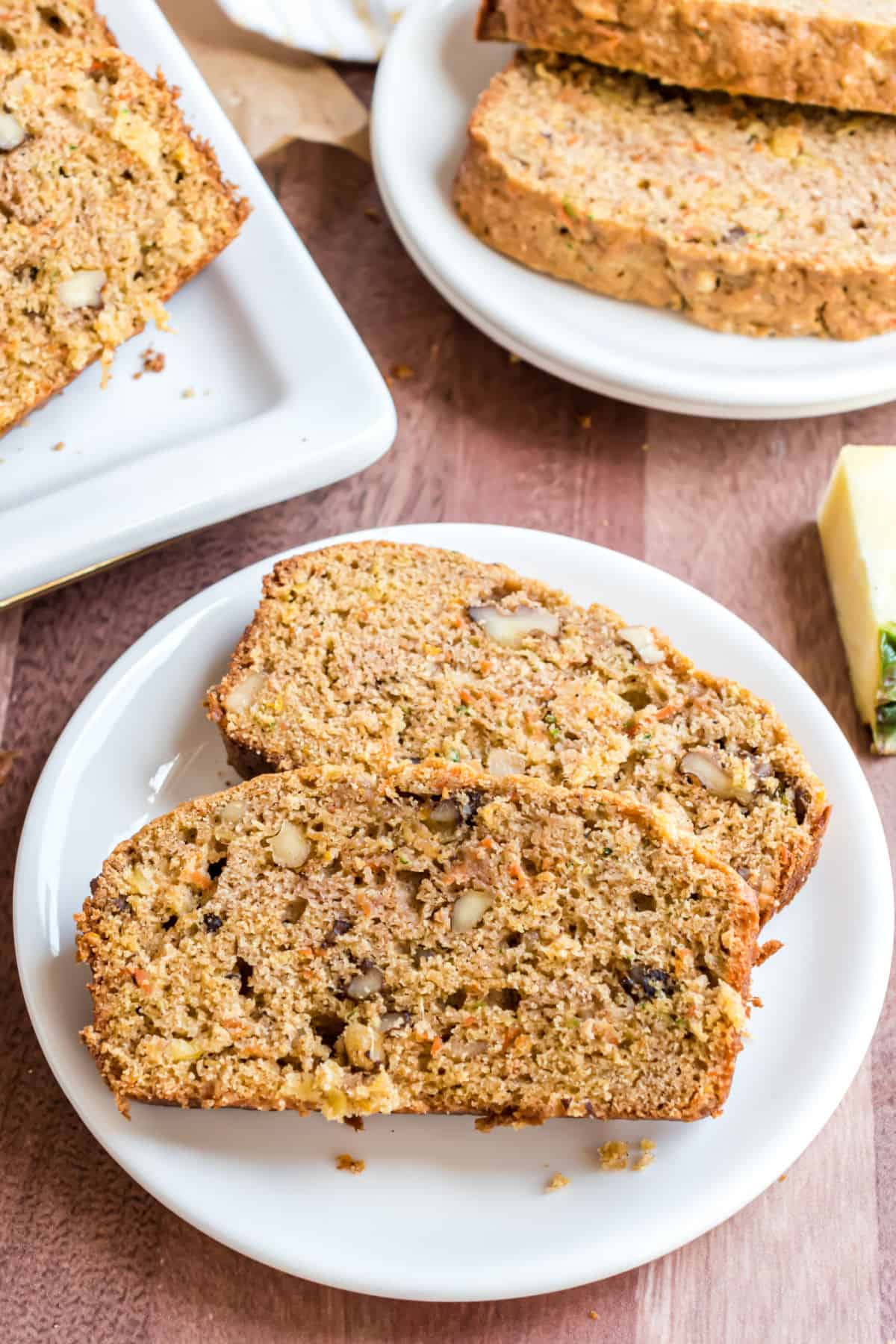 Two slices of pineapple zucchini bread with carrots and walnuts on a white plate.