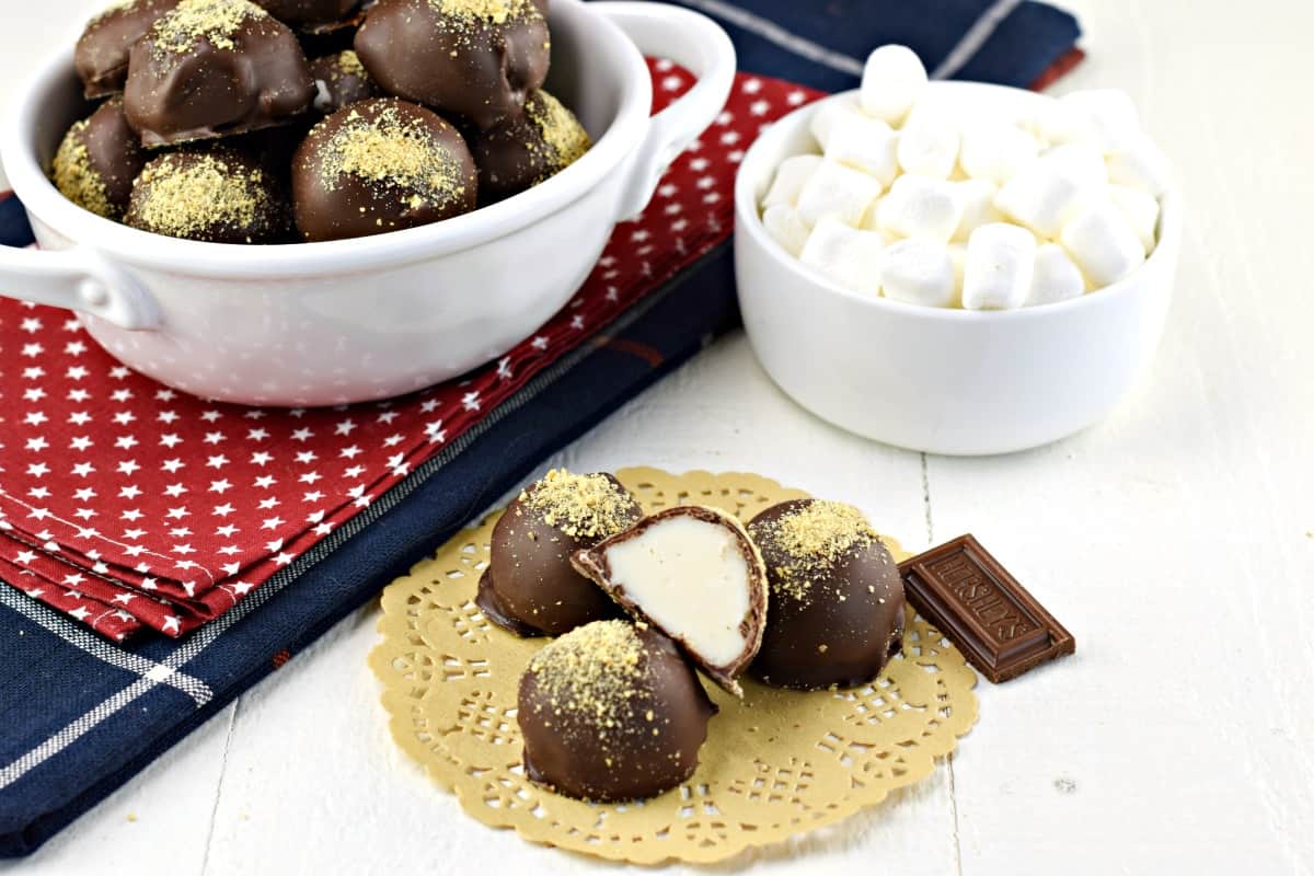 S'mores truffles on a paper doily, with a bowl of marshmallows in background.