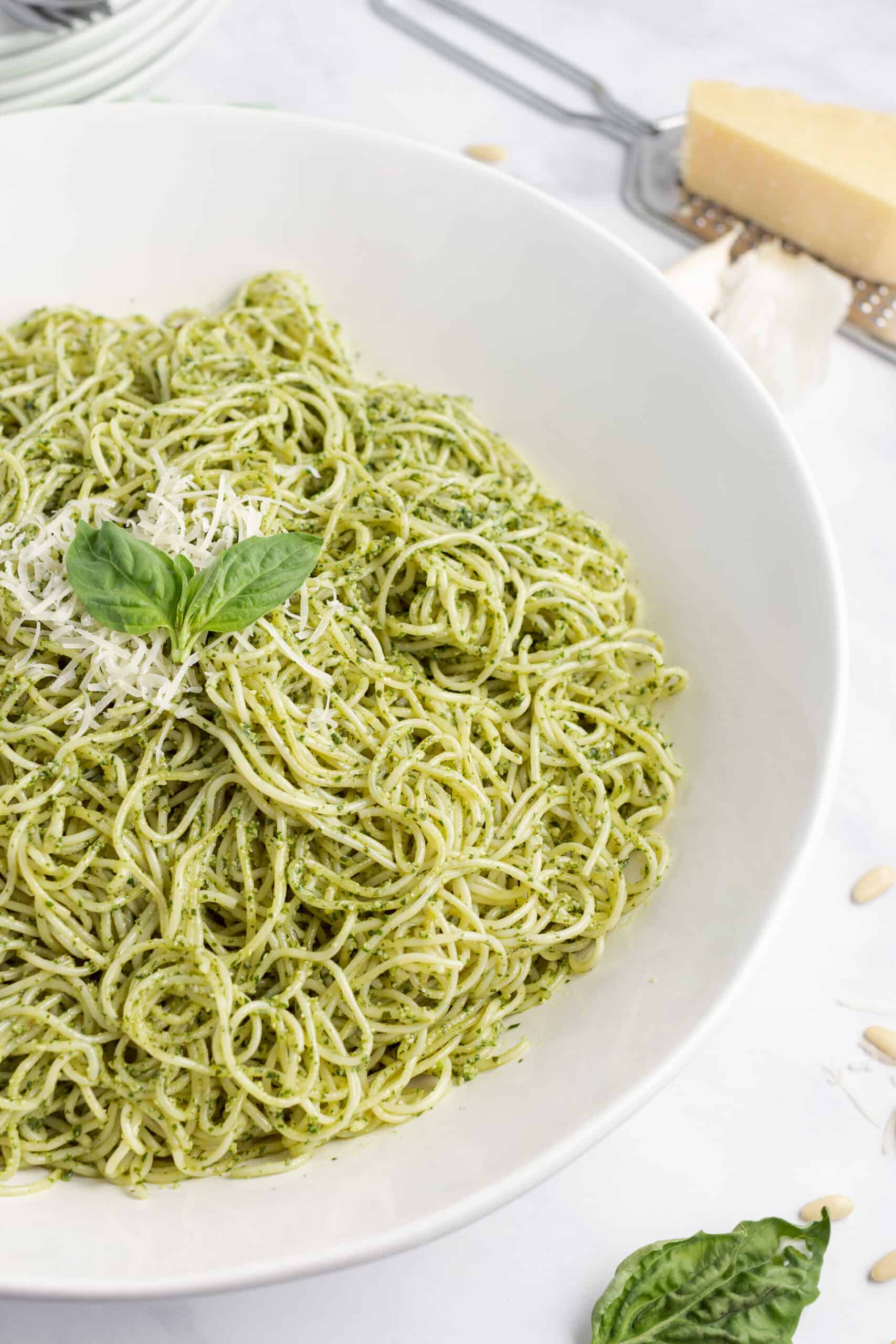 Spaghetti noodles with homemade pesto and parmesan cheese in a white serving bowl.