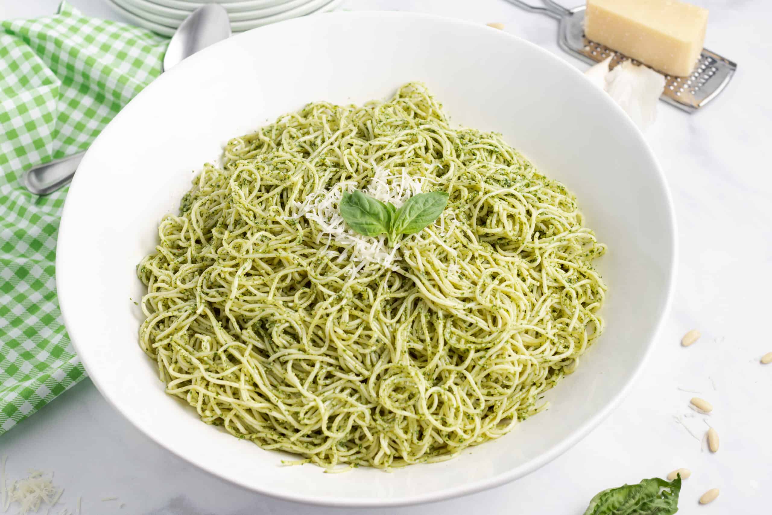 Pesto pasta with parmesan cheese in a white serving bowl and cheese grater on the side.