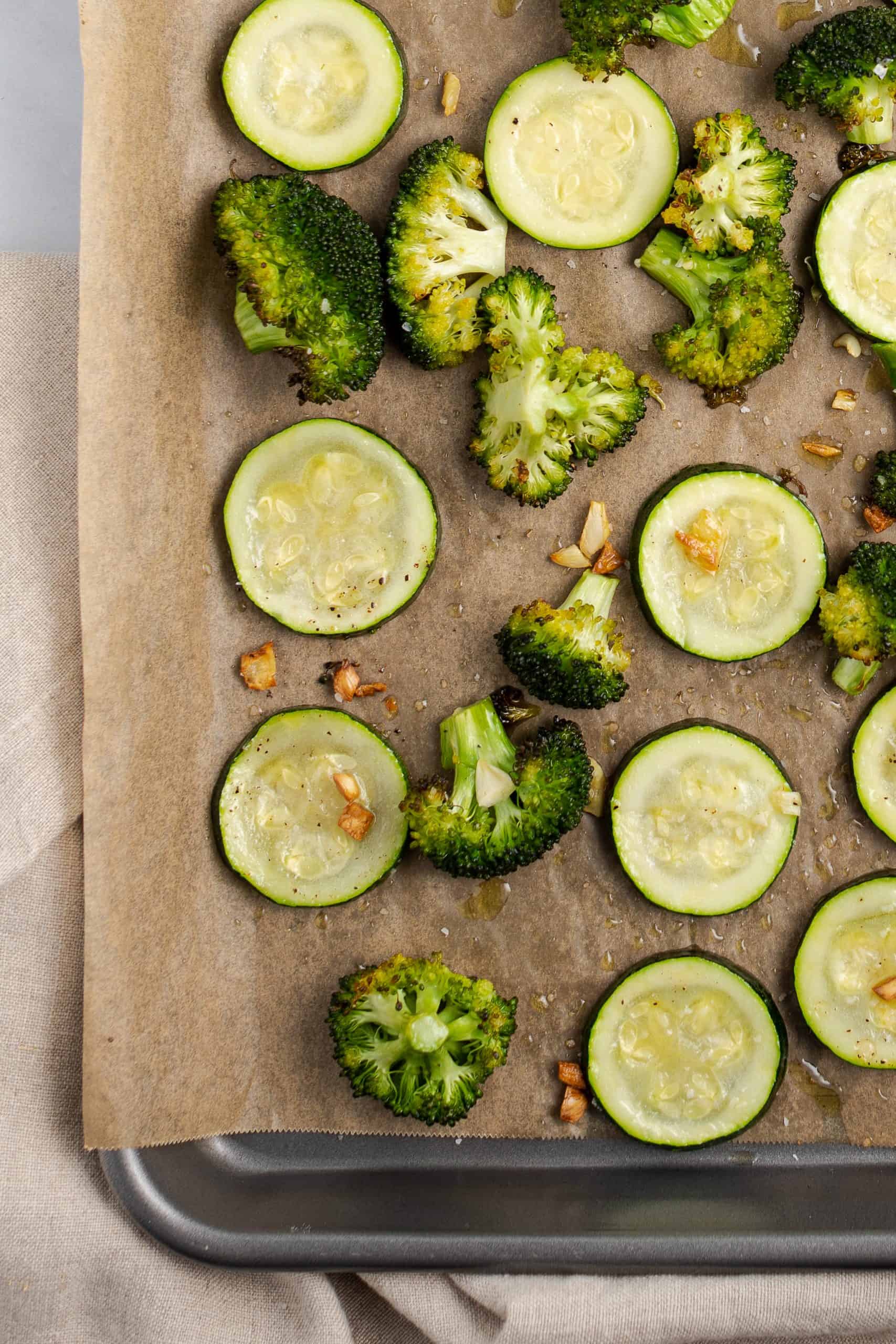 Parchment paper covered sheet pan with roasted broccoli and zucchini with fresh garlic.