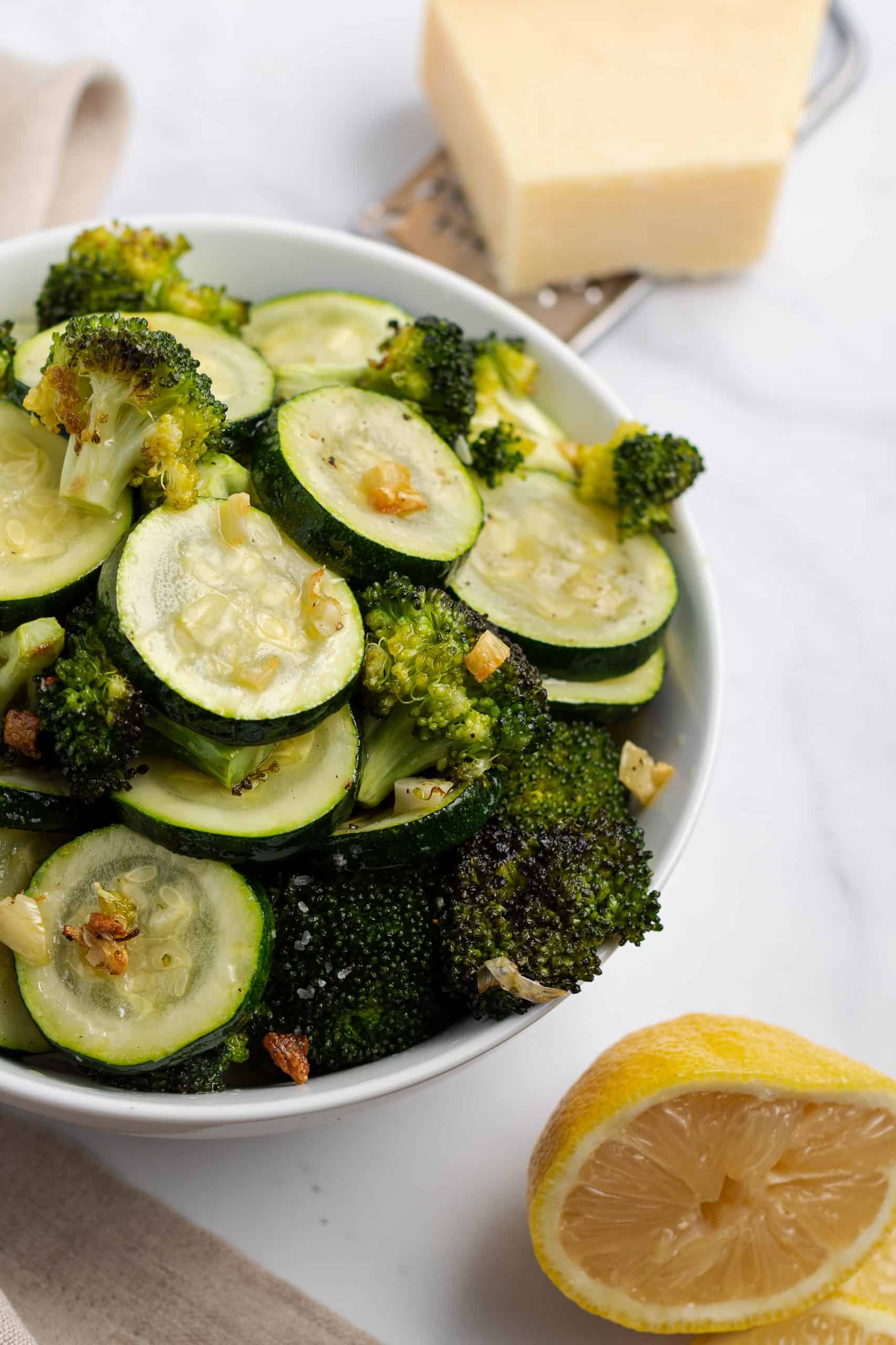 White serving bowl with sliced zucchini and broccoli florets that were roasted and topped with garlic and parmesan cheese.