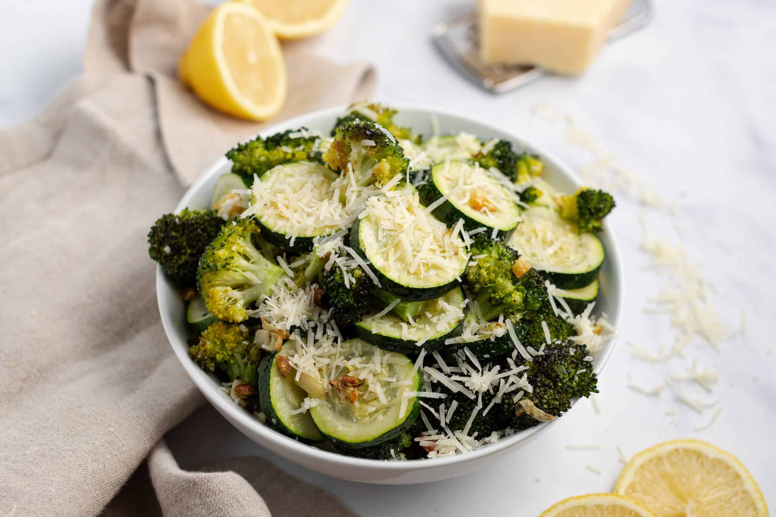 Bowl of roasted broccoli and zucchini topped with lemon juice and parmesan cheese.