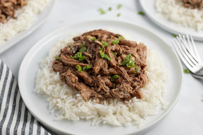 White plate with white rice and shredded pork with green onions.