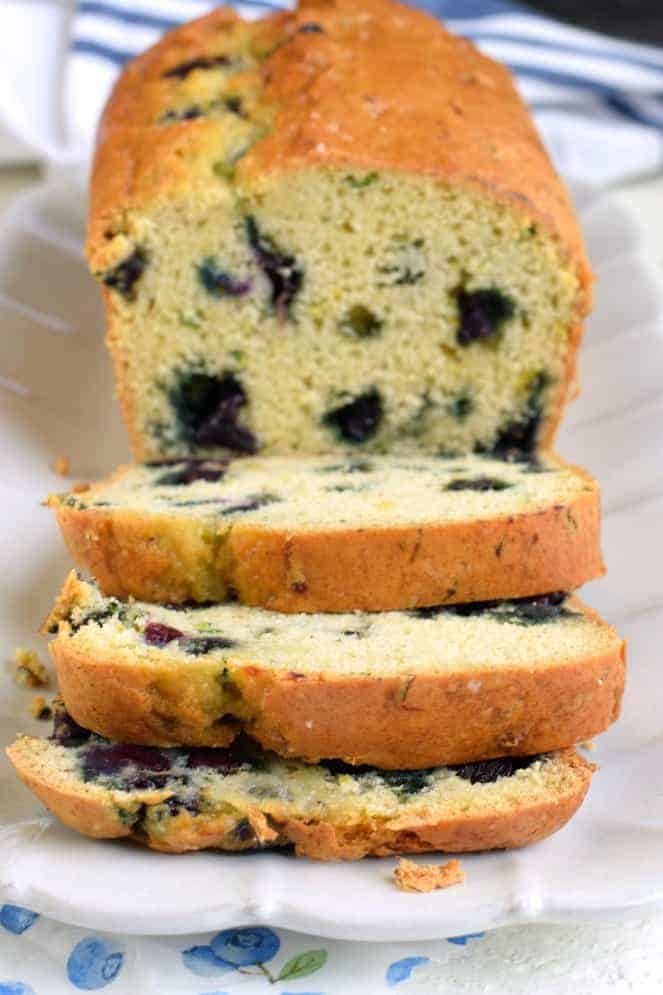 Loaf of zucchini blueberry bread sliced on a white serving plate.