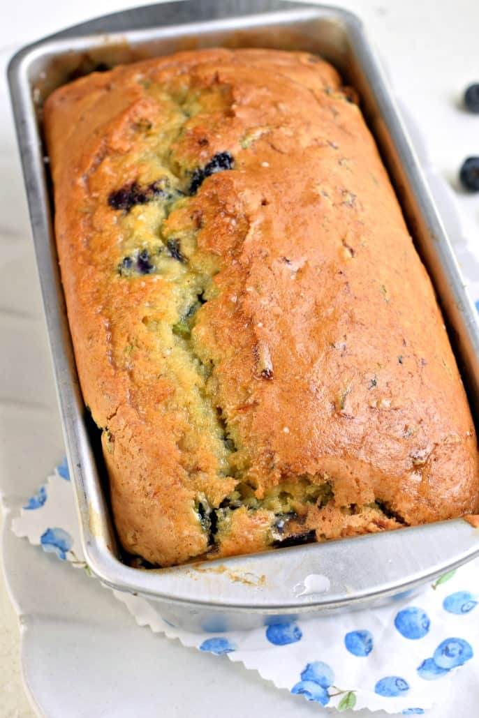 Baked loaf of zucchini blueberry bread in metal loaf pan.