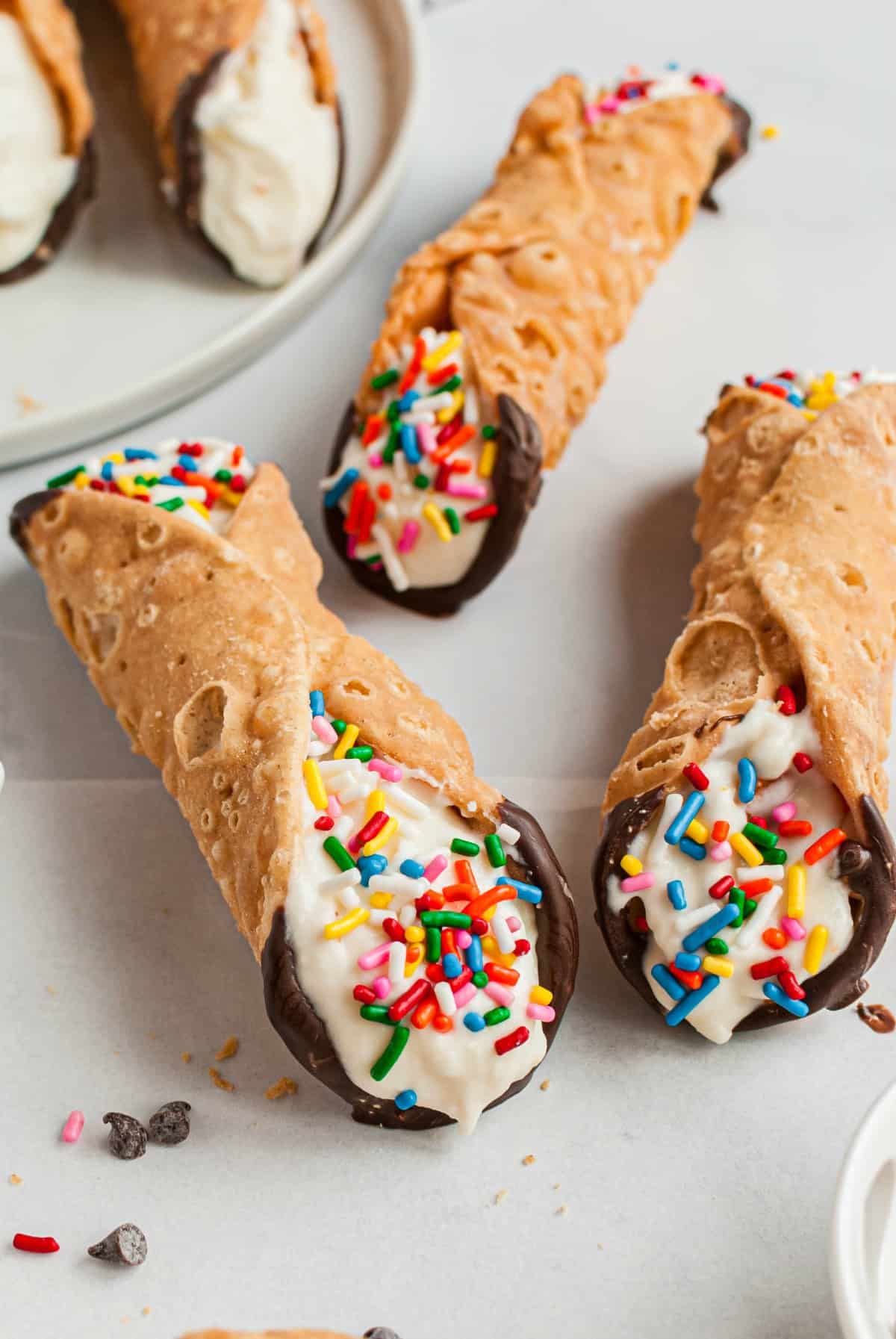 Three cannolis dipped in chocolate and topped with sprinkles.
