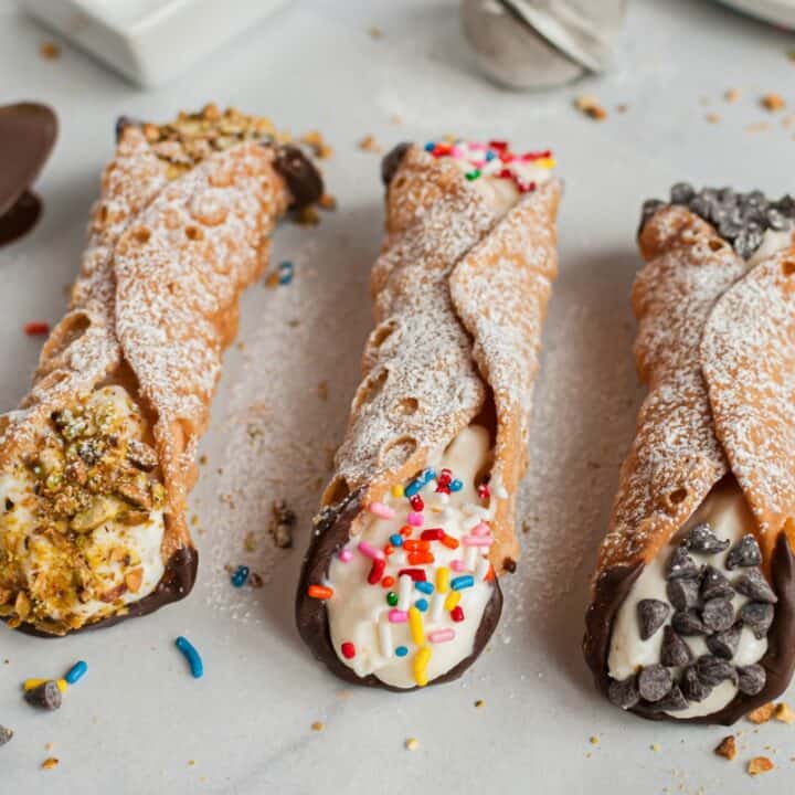 Three cannolis with shells dipped in chocolate and topped with powdered sugar.