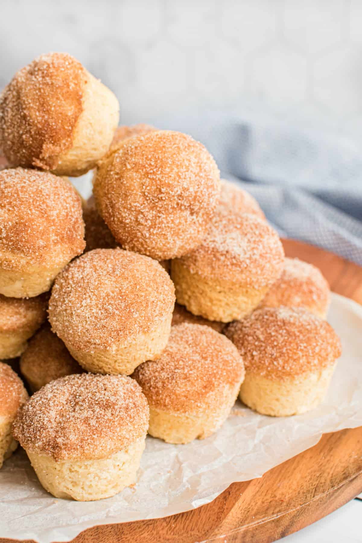 Stack of mini cinnamon muffins on a piece of parchment paper covering a wooden serving board.