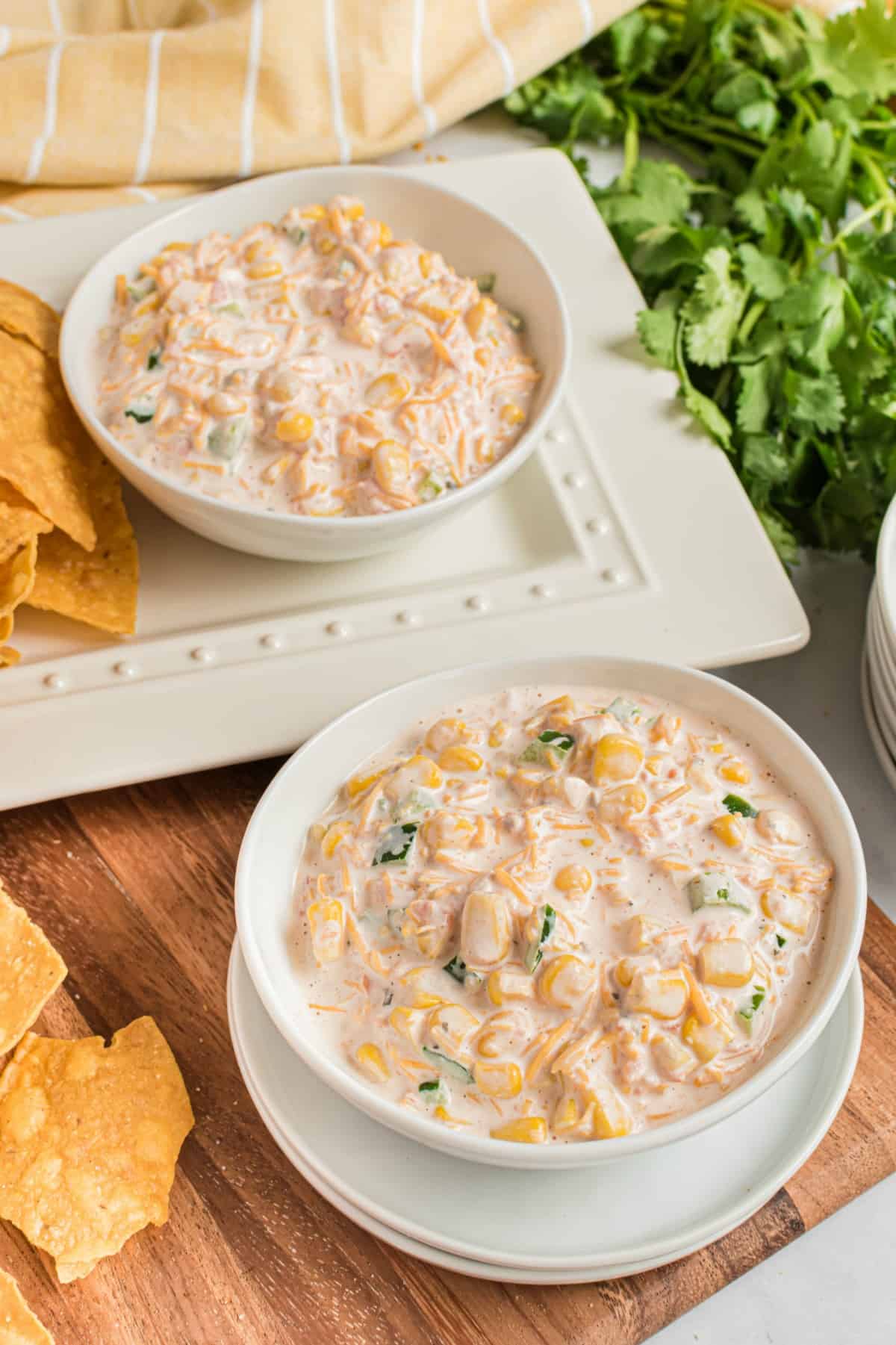 Two white bowls filled with creamy jalapeno corn dip with a side of tortilla chips.