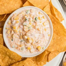 Jalapeno corn dip in a white bowl and a platter of tortilla chips.