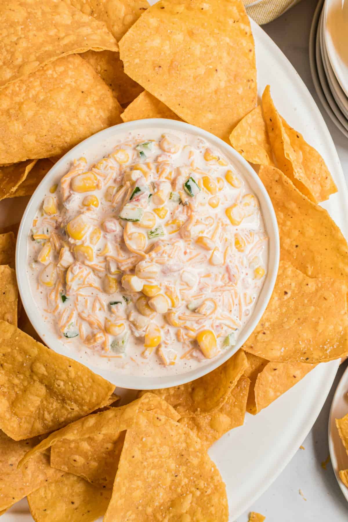 Jalapeno-Mais-Dip in einer weißen Schale und ein Teller mit Tortilla-Chips.