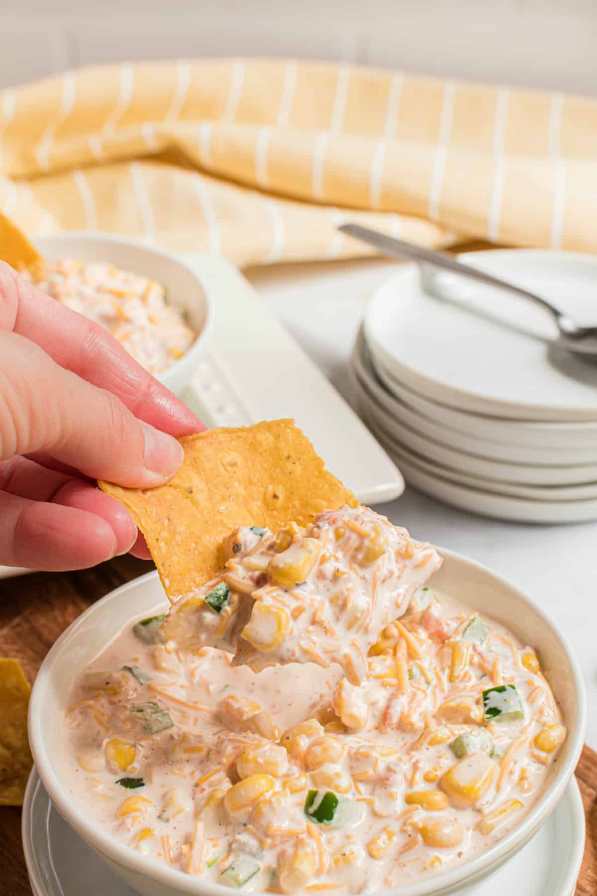 White bowl with corn dip and a tortilla chip being scooped in the dip.