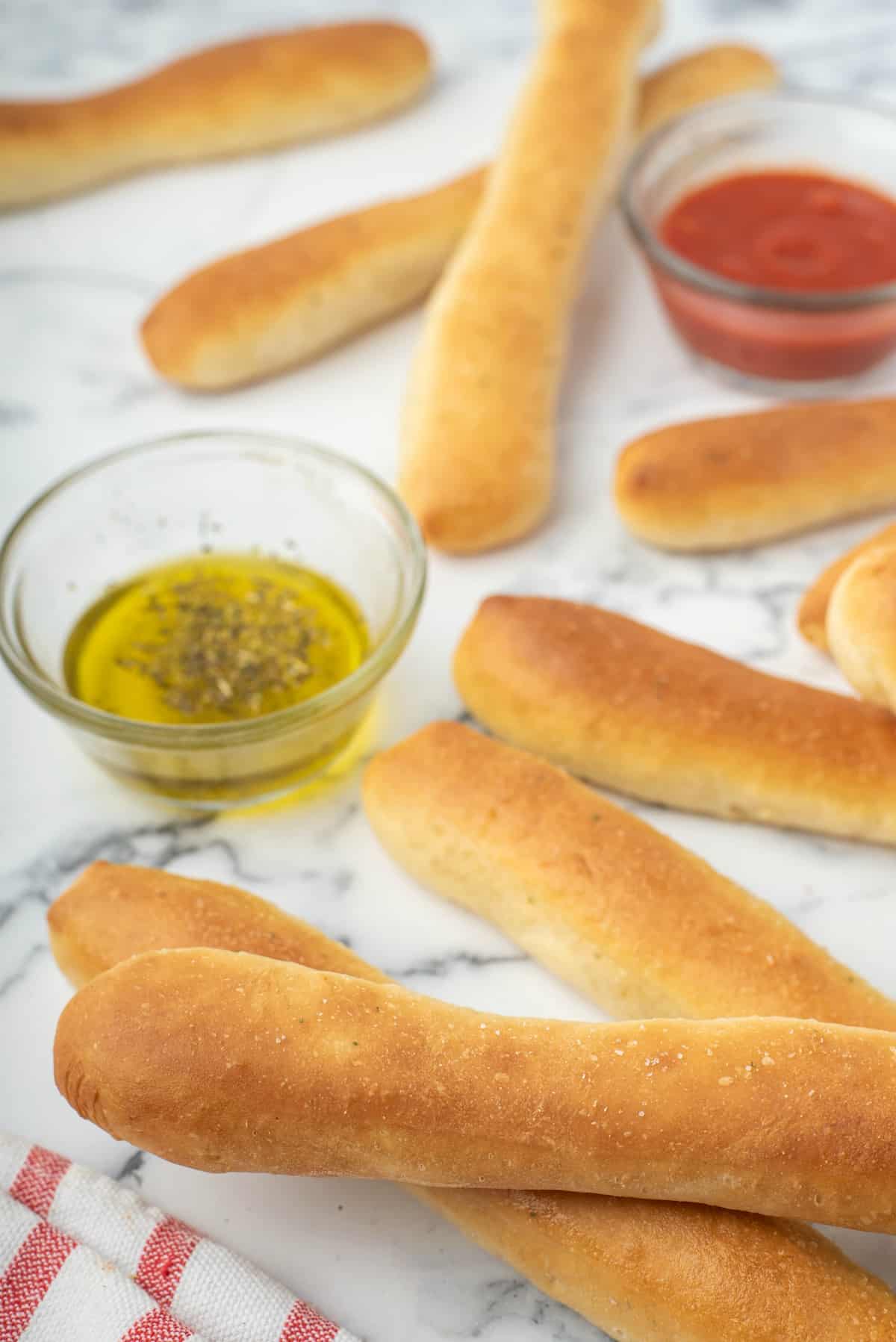 Marble counter with breadsticks laying on top with small bowls of marinara and oil.