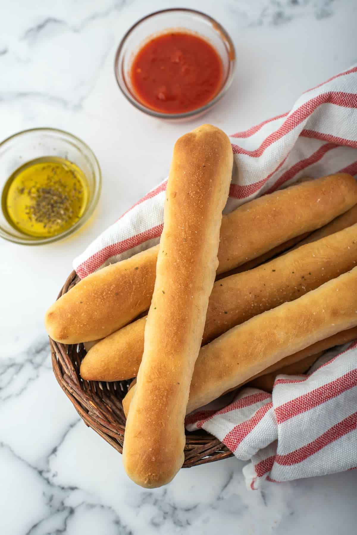 Breadsticks in a wooden bowl with dipping bowls of marinara and oil on the side.