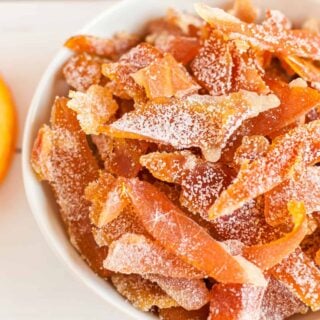 Slices of orange peel coated in sugar in a white bowl.