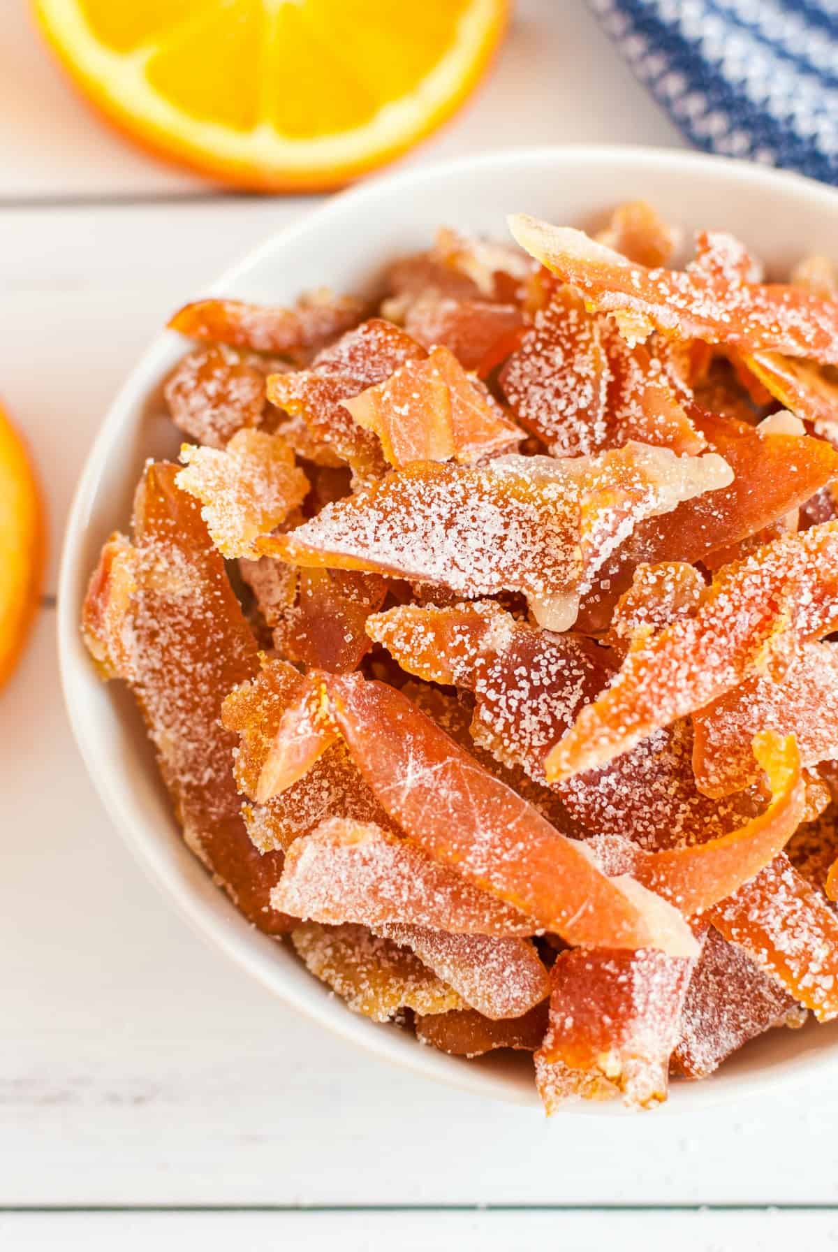 Slices of orange peel coated in sugar in a white bowl.