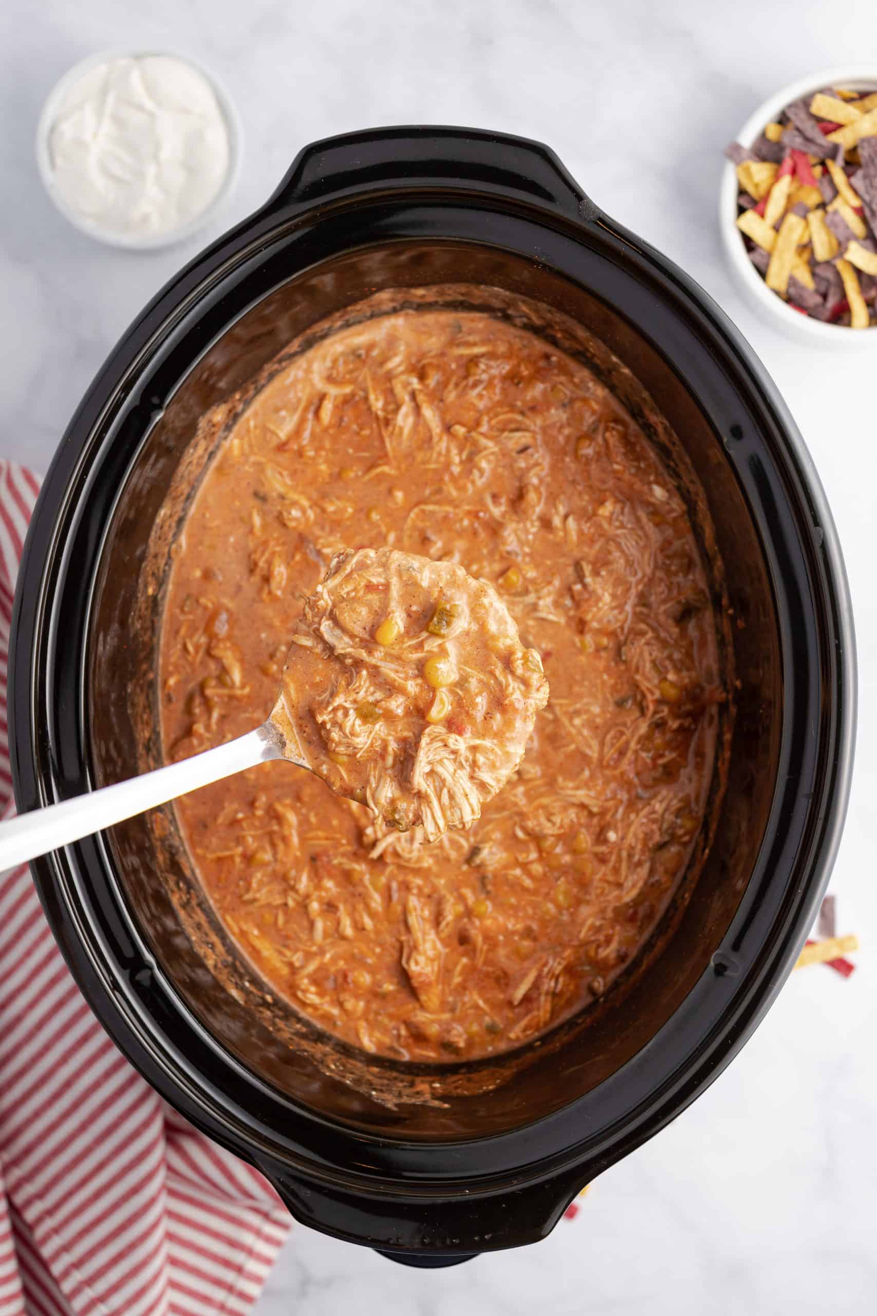 Creamy chicken taco soup in a black crockpot being ladled out.