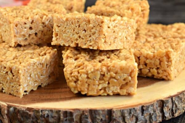 Wooden cake plate piled up with squares of biscoff flavored rice crispy treats