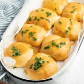 8 chicken pillows wrapped in crescent rolls and lined up in a 13x9 baking dish. Topped with gravy and parsley.