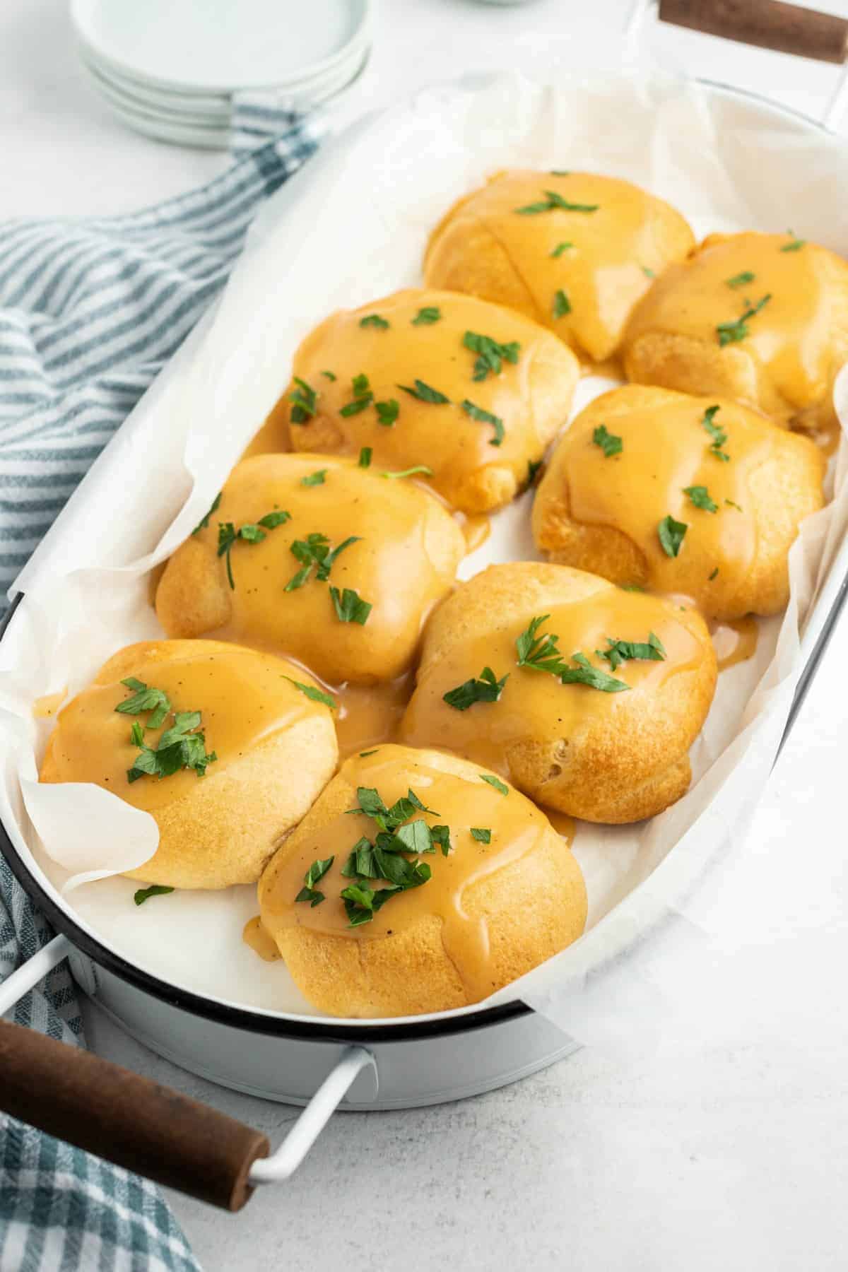 8 chicken pillows wrapped in crescent rolls and lined up in a 13x9 baking dish. Topped with gravy and parsley.