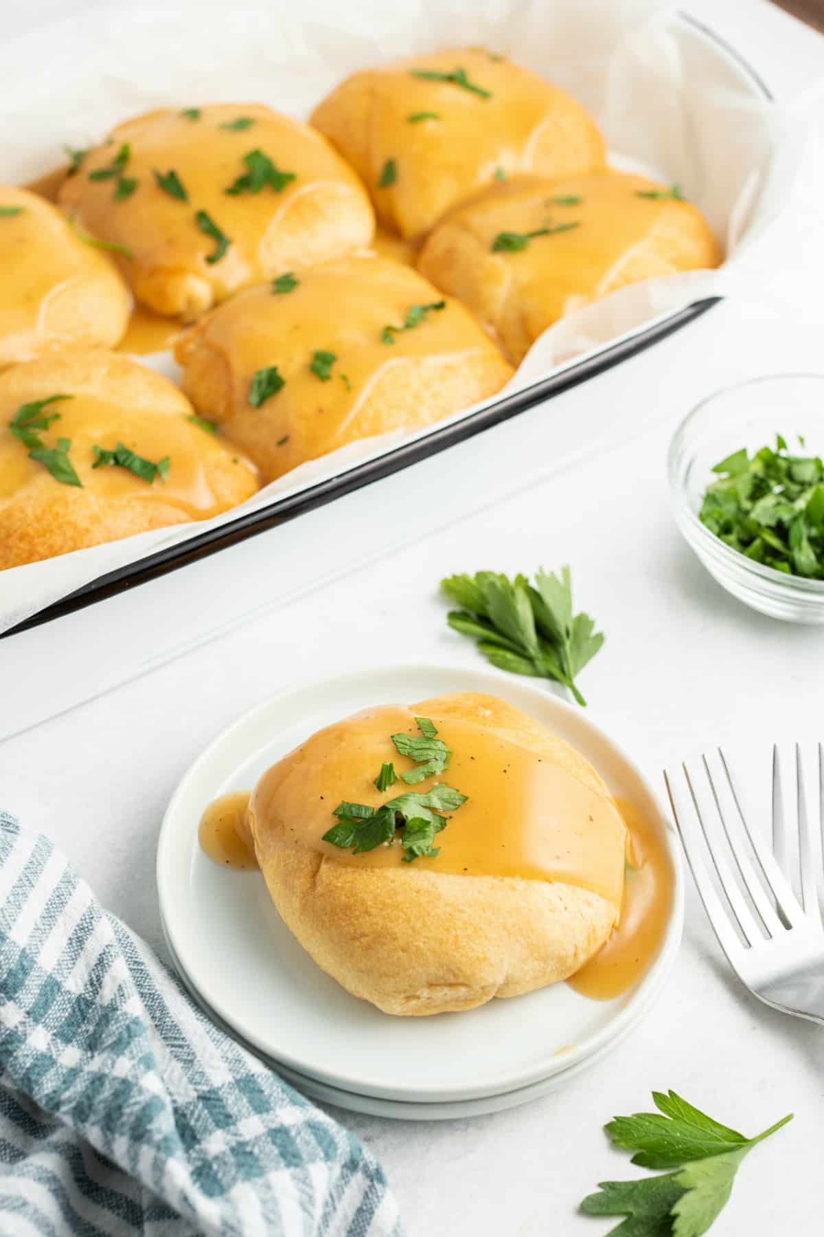 Chicken pillow on a white plate topped with gravy. Pan of chicken kisses in background.