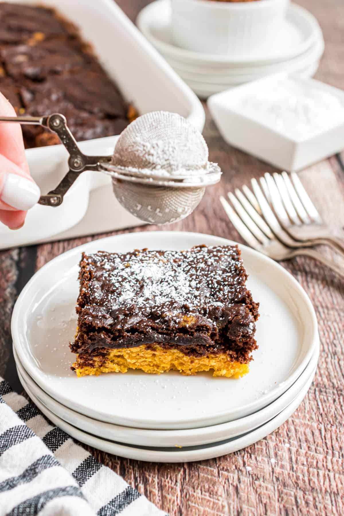 Slice of chocolate pumpkin cake with two layers sprinkled with powdered sugar on a stack of white plates.