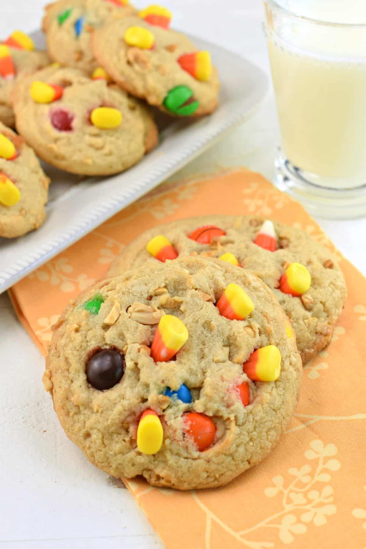 Pay Day cookies with peanuts, m&M's and candy corn, stacked on a light orange linen.