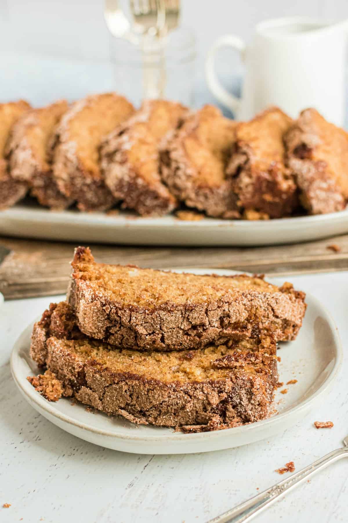 Two slices of amish bread on a white plate with a loaf of bread sliced in the back.